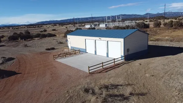 Cream steel garage with a blue roof and trim, three roll-up doors and a concrete apron, mountains behind.