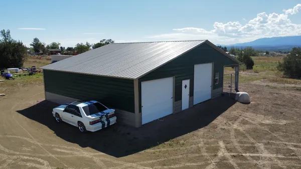 Green steel garage with a gray roof, two white roll-up doors and a car parked out front, aerial view.