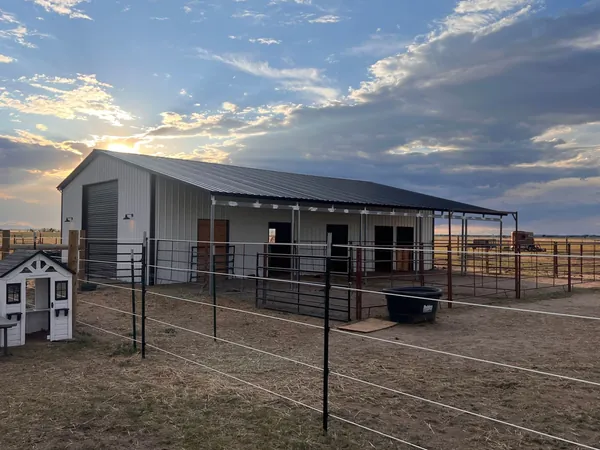 White steel horse barn with a black roof and a long covered lean-to over the stall runs at sunset.