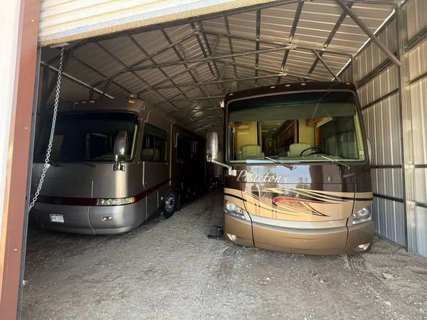 Two motorhomes parked inside a steel RV storage building under the exposed steel roof frame.
