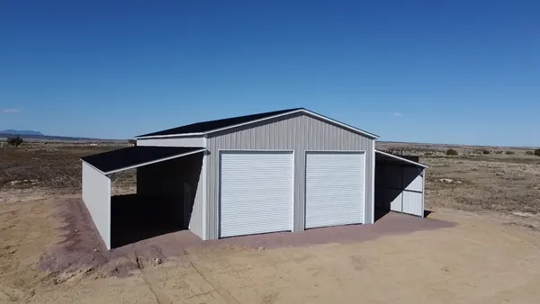 Gray steel building with two white roll-up doors and open lean-to bays on both sides under a clear sky.