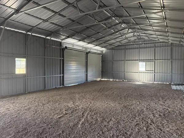 Inside an empty steel building with two roll-up doors, windows and an exposed steel roof frame.