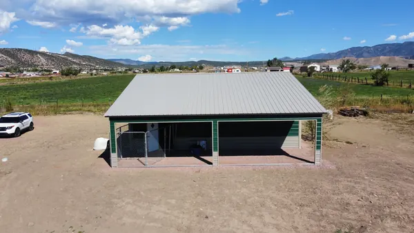 Steel building with a gray roof and a green-framed open-front lean-to, fields and mountains behind.