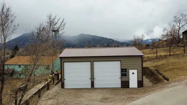 Tan steel garage with a brown roof and two white roll-up doors, snowy foothills in the background.
