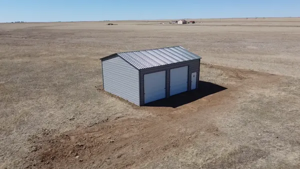 Light gray steel garage with two white roll-up doors standing on open prairie, aerial view.
