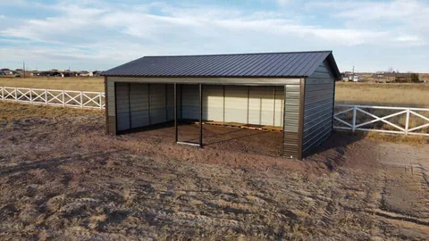 Charcoal steel barn with one open side next to a white pasture fence