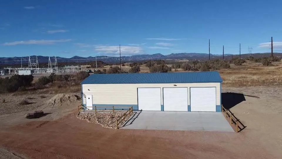Front view of a 24x60 cream steel garage with blue trim and three roll-up doors