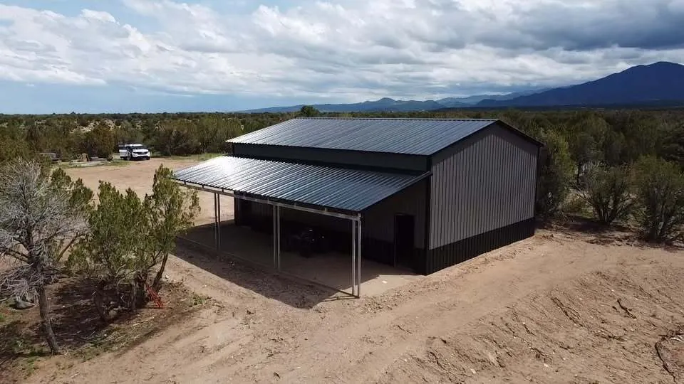 Charcoal steel building with a covered lean-to along its side on a cleared lot