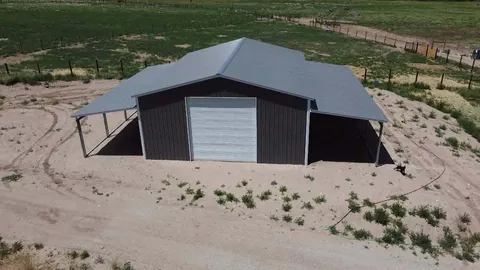 Charcoal steel shop with a white roll-up door and lean-tos on both sides on open ground