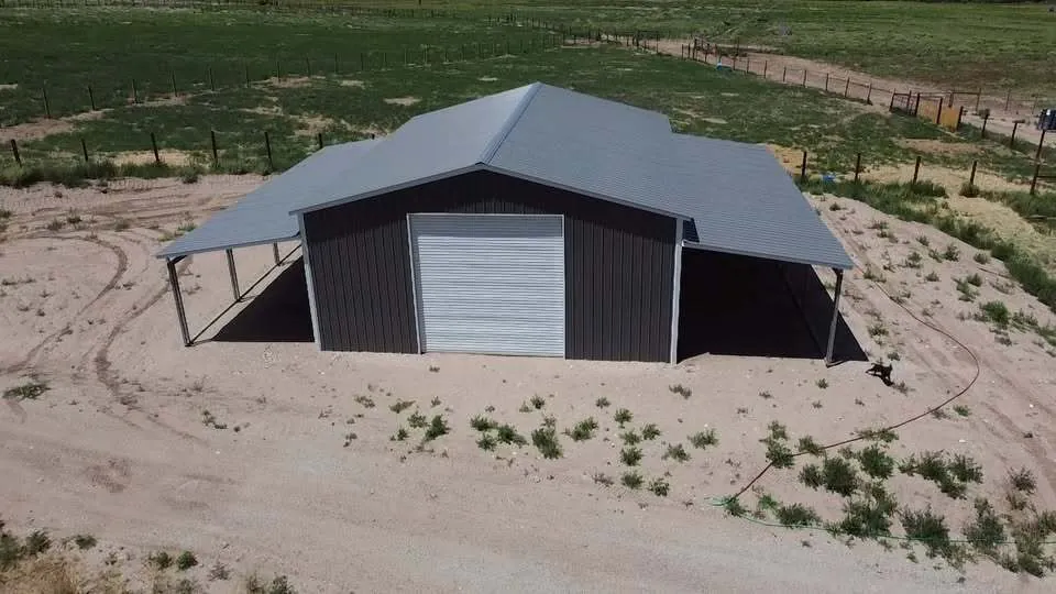 Charcoal steel shop with a white roll-up door and lean-tos on both sides on open ground