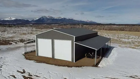 Gray steel building with two roll-up doors and full-length lean-tos in snow, peaks behind