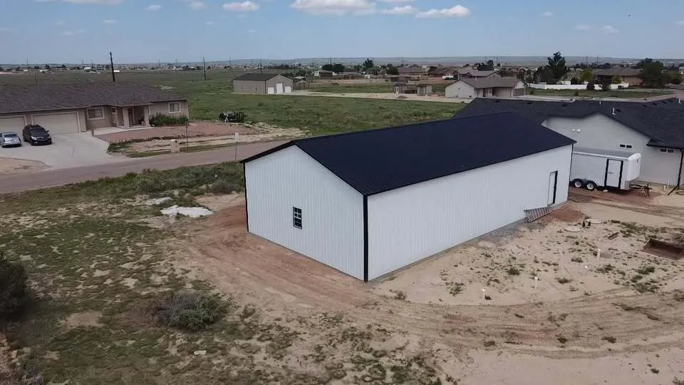 White steel building with a black roof on a rural lot, aerial view