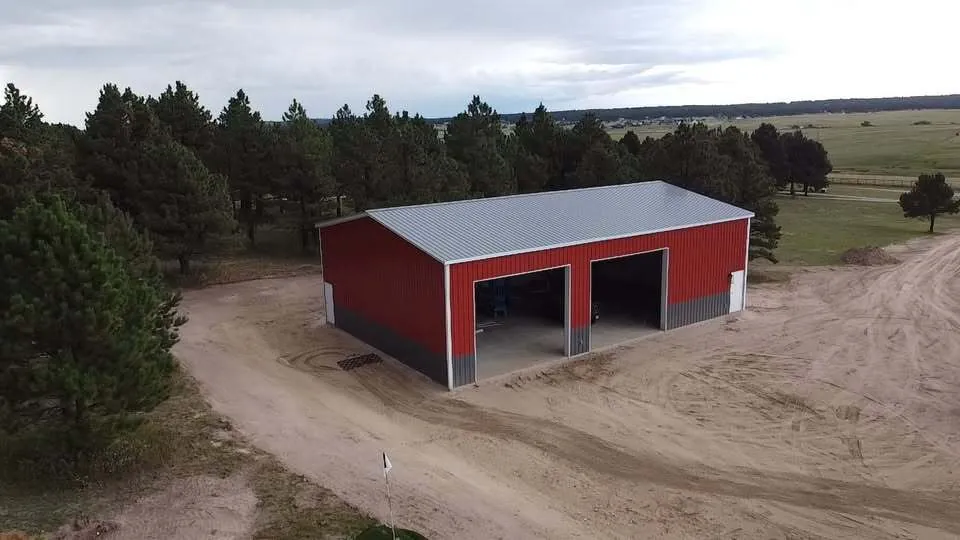 Red 40x60 steel shop in a pine clearing, aerial view
